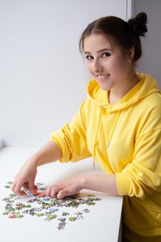 pretty brunette girl in yellow hoodie arranging pieces of a Jigsaw Puzzle Game in bright white room. playing board game home