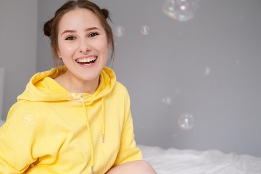 portrait of charming young woman in yellow among soap bubbles on bright grey background. fashionable teenager. trendy colours