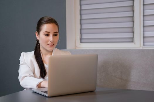 woman sitting by the table on couch in grey room - office and use laptop. big boss. important, confident women. femininity. millennials.