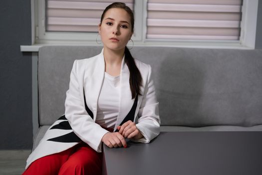 sexy business woman sitting by the table on couch in grey room - office. big boss. important, confident women. femininity. millennials.