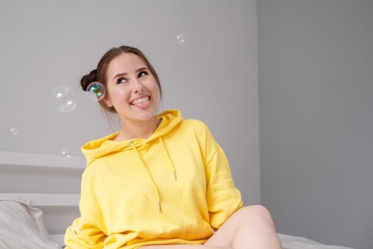 woman in yellow among soap bubbles on grey background.