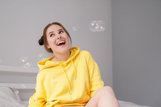 portrait of charming young woman in yellow among soap bubbles on bright grey background. fashionable teenager. trendy colours