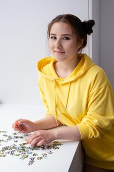 pretty brunette girl in yellow hoodie arranging pieces of a Jigsaw Puzzle Game in bright white room. playing board game home