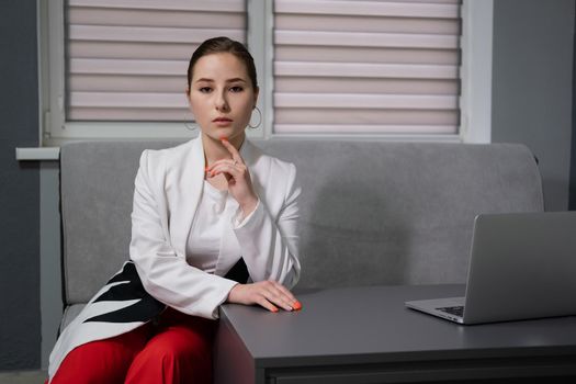 sexy business woman sitting by the table on couch in grey room - office. big boss. important, confident women. femininity. millennials.