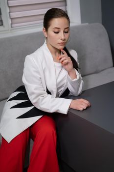 beautiful business woman in red pants, white blouse and Blazer sitting by the table on couch in grey room office.