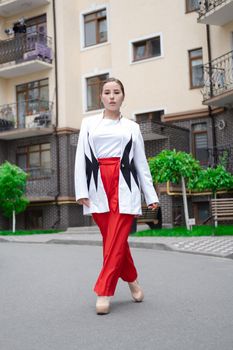 business woman in red pants, white blouse and jacket walking by the street.