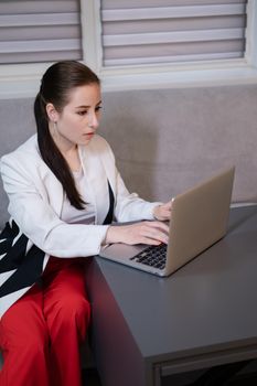 brunette woman use laptop in grey room. freelancer. working from home. student, remote study.