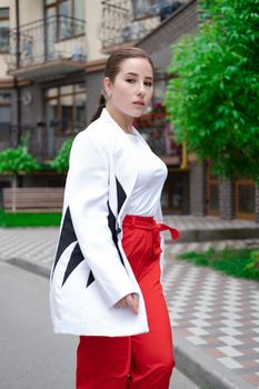 business woman in red pants, white blouse and jacket walking by the street.