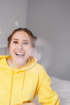 portrait of charming young woman in yellow among soap bubbles on bright grey background. fashionable teenager. trendy colours