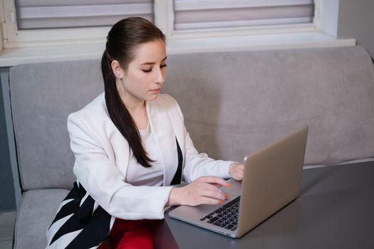 brunette woman use laptop in grey room. freelancer. working from home. student, remote study.