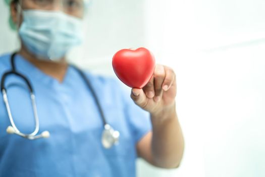 Asian doctor wearing face shield and PPE suit new normal to protect safety infection Covid-19 Coronavirus holding red heart in hand at hospital.