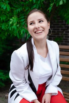 sexy confident brunette woman in red and white outdoors sitting on bench.