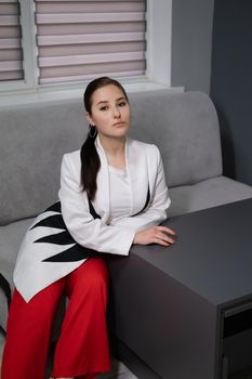 sexy business woman sitting by the table on couch in grey room - office. big boss. important, confident women. femininity. millennials.