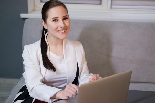 woman sitting by the table on couch in grey room - office and use laptop. big boss. important, confident women. femininity. millennials.