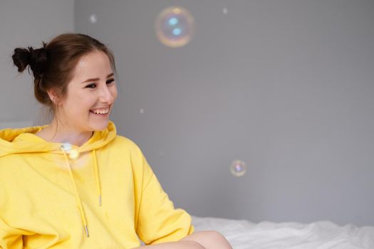 portrait of charming young woman in yellow among soap bubbles on bright grey background. fashionable teenager. trendy colours