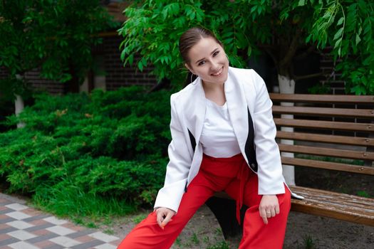 sexy confident brunette woman in red and white outdoors sitting on bench.