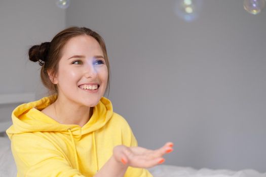 portrait of charming young woman in yellow among soap bubbles on bright grey background. fashionable teenager. trendy colours