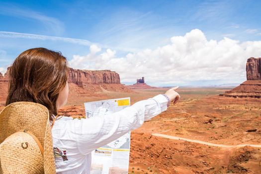 Back side of girl wearing straw hat searching right direction on map in Monument Valley, Utah, USA