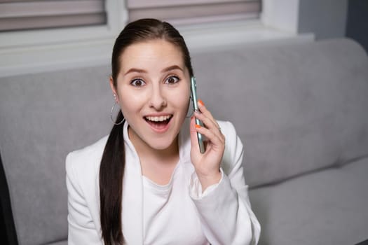 portrait of happy, surprised, excited brunette business woman talking by phone in gray office. gain, good phone call. success, victory, present.