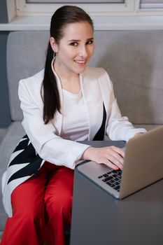 woman sitting by the table on couch in grey room - office and use laptop. big boss. important, confident women. femininity. millennials.