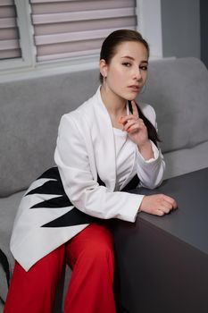 sexy business woman sitting by the table on couch in grey room - office. big boss. important, confident women. femininity. millennials.