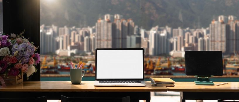 Mockup laptop computer with blank white screen on workplace, cargo port and building background.