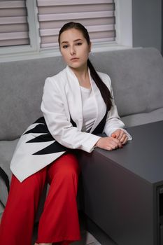 sexy business woman sitting by the table on couch in grey room - office. big boss. important, confident women. femininity. millennials.