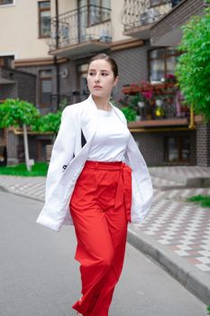business woman in red pants, white blouse and jacket walking by the street.