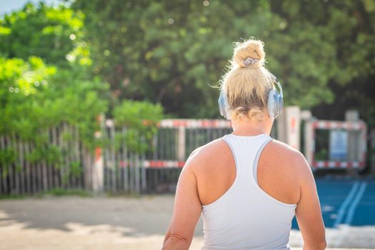 Fitness woman listening to music in sportswear with wireless in-ear headphones on summer ocean beach