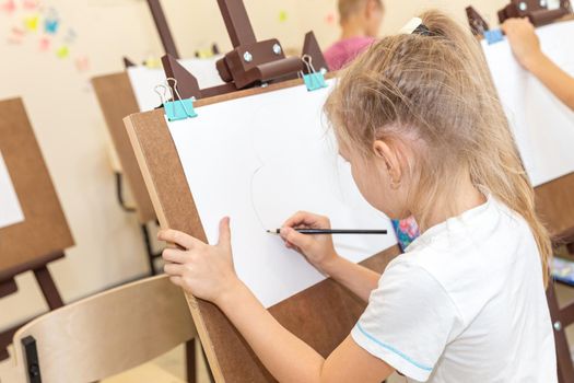 Little girl painting picture on easel in classroom