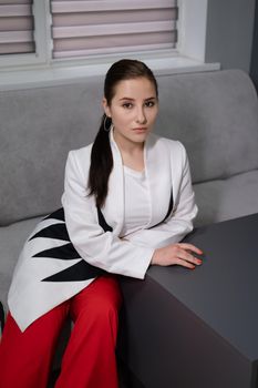 sexy business woman sitting by the table on couch in grey room - office. big boss. important, confident women. femininity. millennials.