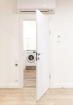 White opened door in modern home with air conditioner and wooden floor