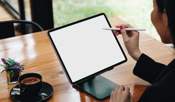 Side view of female freelancer holding stylus pen pointing on screen of digital tablet with blank white screen.