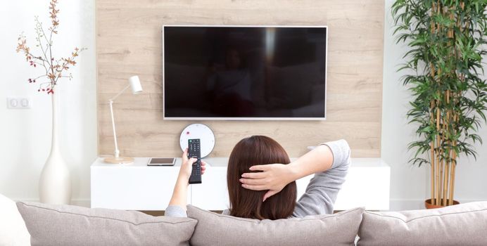 Young woman watching TV in living room, back view