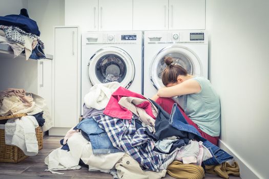 Unhappy Stressed Woman with Pile Of Clothes Near Washing Machine in laundry