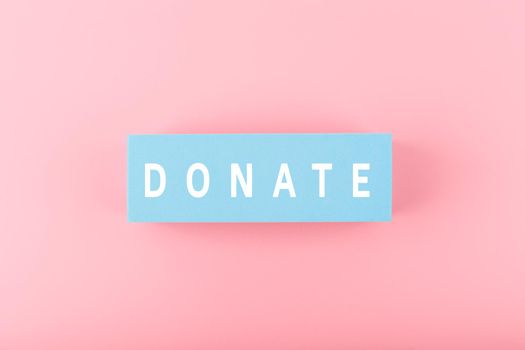 Donation or charity modern minimal concept. Single word donate written on light blue block against bright pink background. 