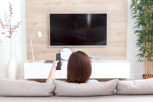Young woman watching TV in living room, back view