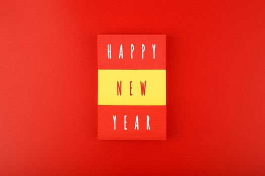 Happy New Year bright red minimal trendy concept. Modern composition with red and yellow toy blocks with written Happy New Year text against red background with copy space. Minimalistic postcard