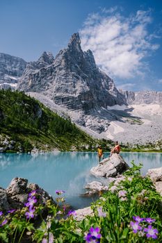 Morning with clear sky on Lago di Sorapis in the Italian Dolomites, milky blue lake Lago di Sorapis, Lake Sorapis, Dolomites, Italy. Couple man and woman mid age walking by the lake in the mountains 