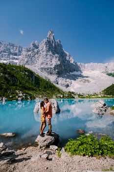 Morning with clear sky on Lago di Sorapis in the Italian Dolomites, milky blue lake Lago di Sorapis, Lake Sorapis, Dolomites, Italy. Couple man and woman mid age walking by the lake in the mountains 