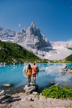 Morning with clear sky on Lago di Sorapis in the Italian Dolomites, milky blue lake Lago di Sorapis, Lake Sorapis, Dolomites, Italy. Couple man and woman mid age walking by the lake in the mountains 