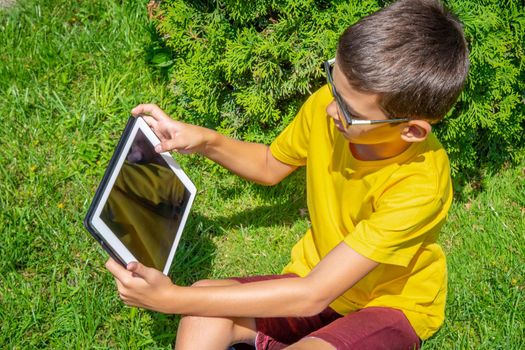 Boy playing with tablet PC on green grass lawn with copy space