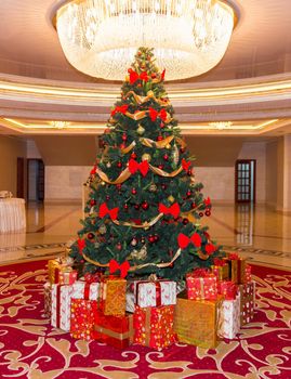 a lot of presents laying next to a beautiful big christmas tree