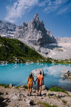 Morning with clear sky on Lago di Sorapis in the Italian Dolomites, milky blue lake Lago di Sorapis, Lake Sorapis, Dolomites, Italy. Couple man and woman mid age walking by the lake in the mountains 