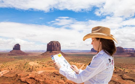 Back side of girl wearing straw hat searching right direction on map in Monument Valley, Utah, USA