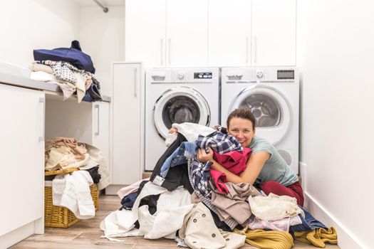 Happy woman in laundry room with a pile of dirty clothes