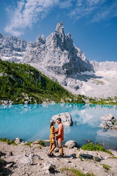 Morning with clear sky on Lago di Sorapis in the Italian Dolomites, milky blue lake Lago di Sorapis, Lake Sorapis, Dolomites, Italy. Couple man and woman mid age walking by the lake in the mountains 