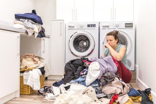 Sad woman sitting in laudry room with a pile of dirty clothes