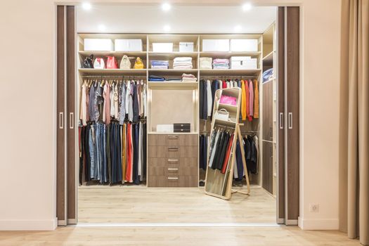 Modern wooden wardrobe with clothes hanging on rail in walk in closet design interior