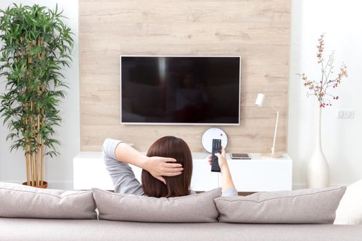 Young woman watching TV in the living room. Back view